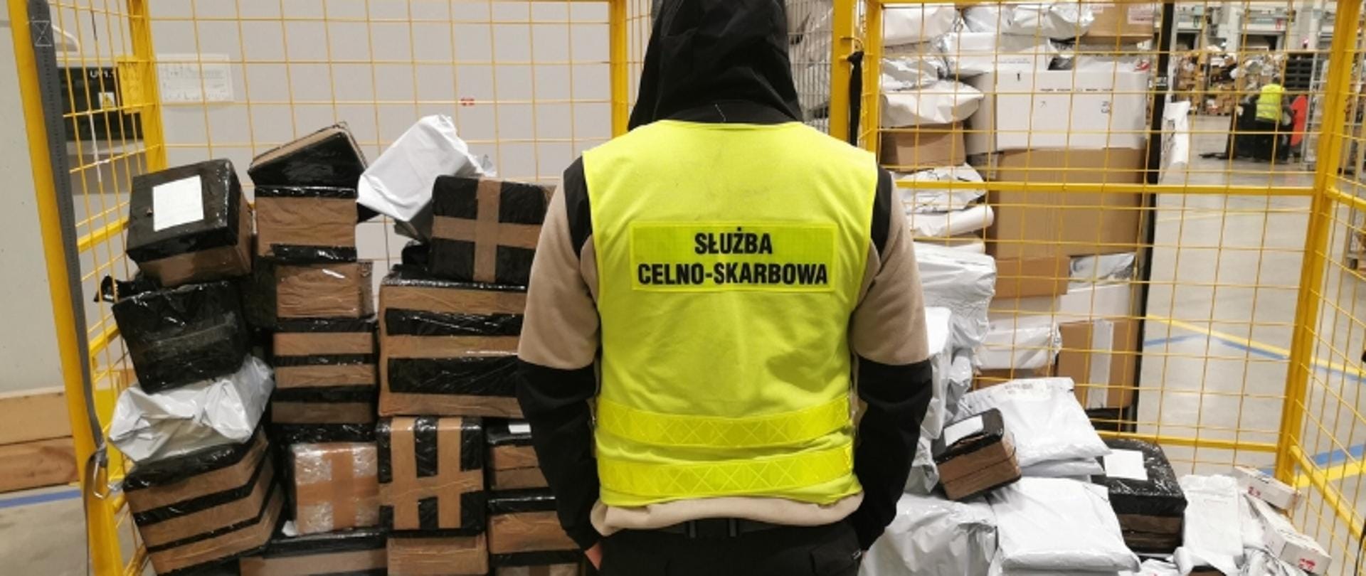 Skaner rentgenowski w akcji, pokazujący wnętrze paczki z widocznymi kształtami e-papierosów, nadzorowany przez funkcjonariuszy KAS.