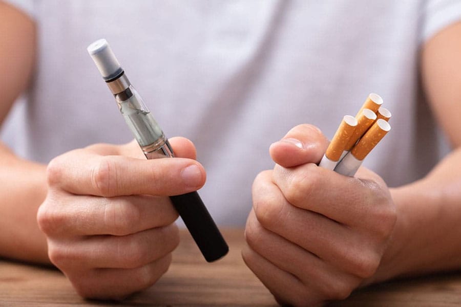 Osoba używająca małego, dyskretnego e-papierosa w swobodnym, towarzyskim otoczeniu, np. na imprezie lub spotkaniu z przyjaciółmi, ilustrująca profil Social Vaper.